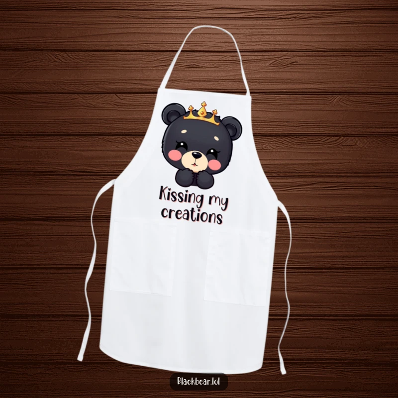 Funny black bear cub apron, a cub in a sparkly crown blowing a kiss downwards, adding sweet humor to kitchen duties.