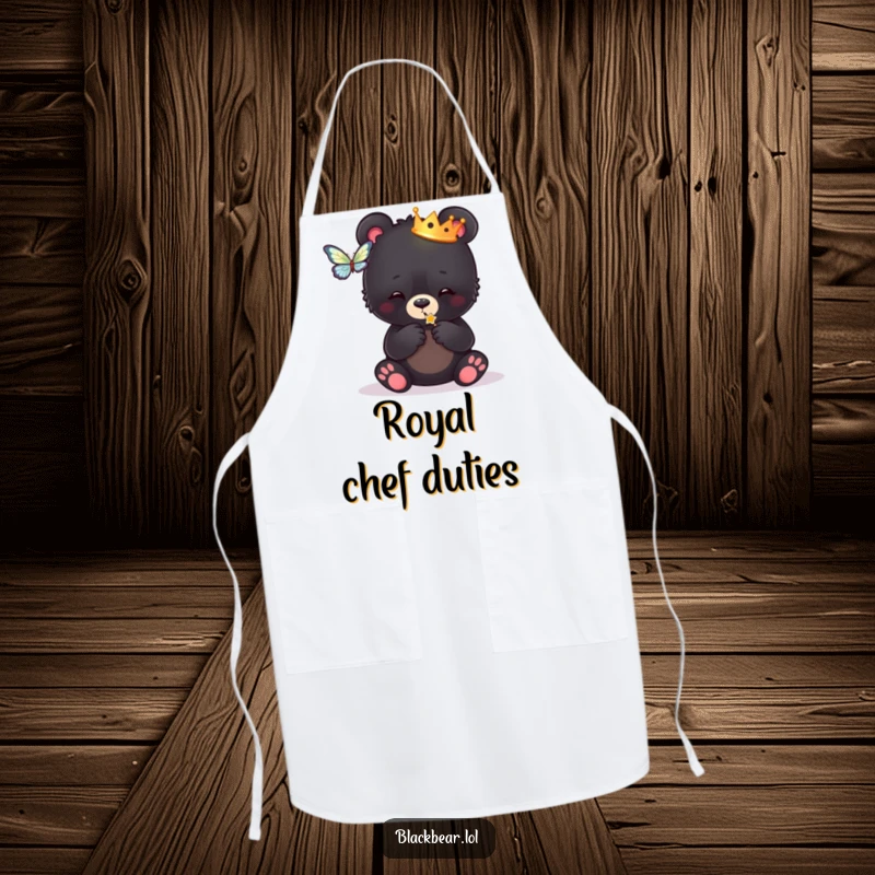 Funny apron showing a black bear cub wearing a crown, playfully batting at a butterfly, ready for culinary kingdom duties.