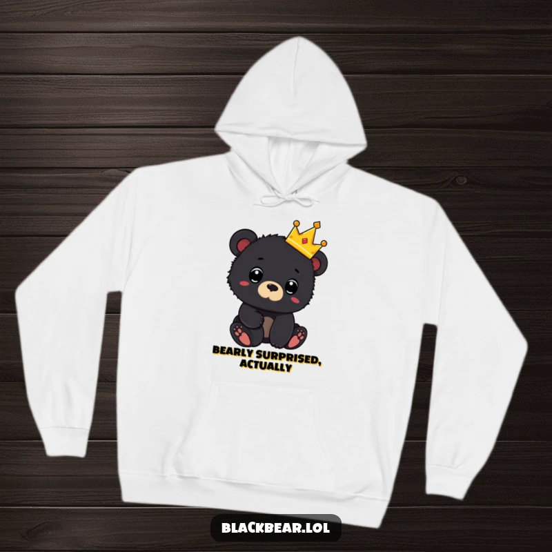 Funny hoodie showing a black bear cub wearing a tiny crown and looking surprised, offering warmth and adorable royal humor.