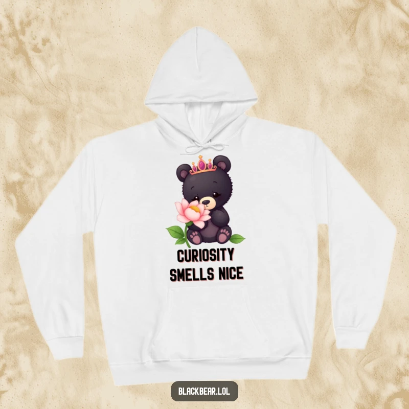 Funny hoodie featuring a black bear cub adorned with a tiara, curiously sniffing a vibrant, oversized flower.