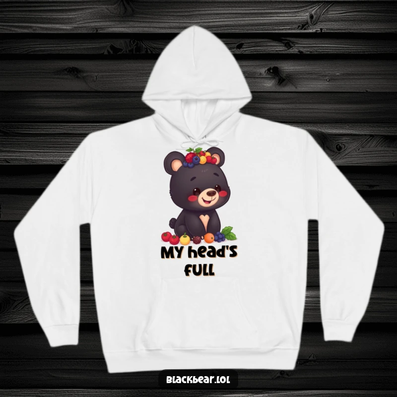 Funny hoodie print of a smiling black bear cub focused on balancing a large pile of berries on its head.