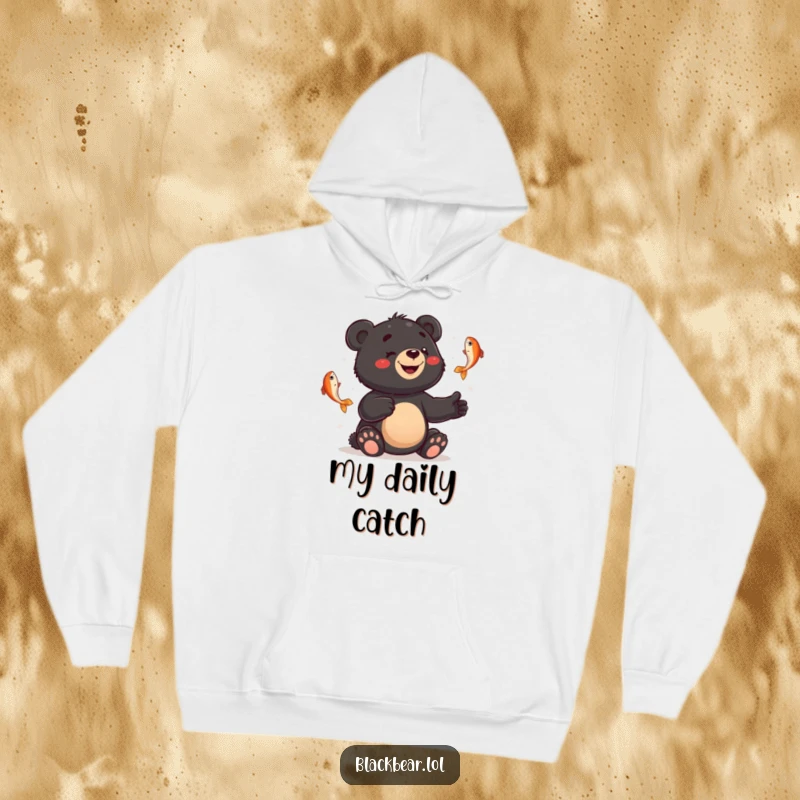 Funny hoodie depicting a smiling black bear cub juggling fish with a bewildered expression, blending warmth with humor.