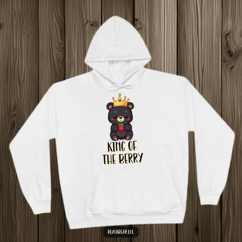 Funny black bear cub hoodie, a royal cub in a crown, balancing a berry on its nose, providing cozy comfort and humorous charm.