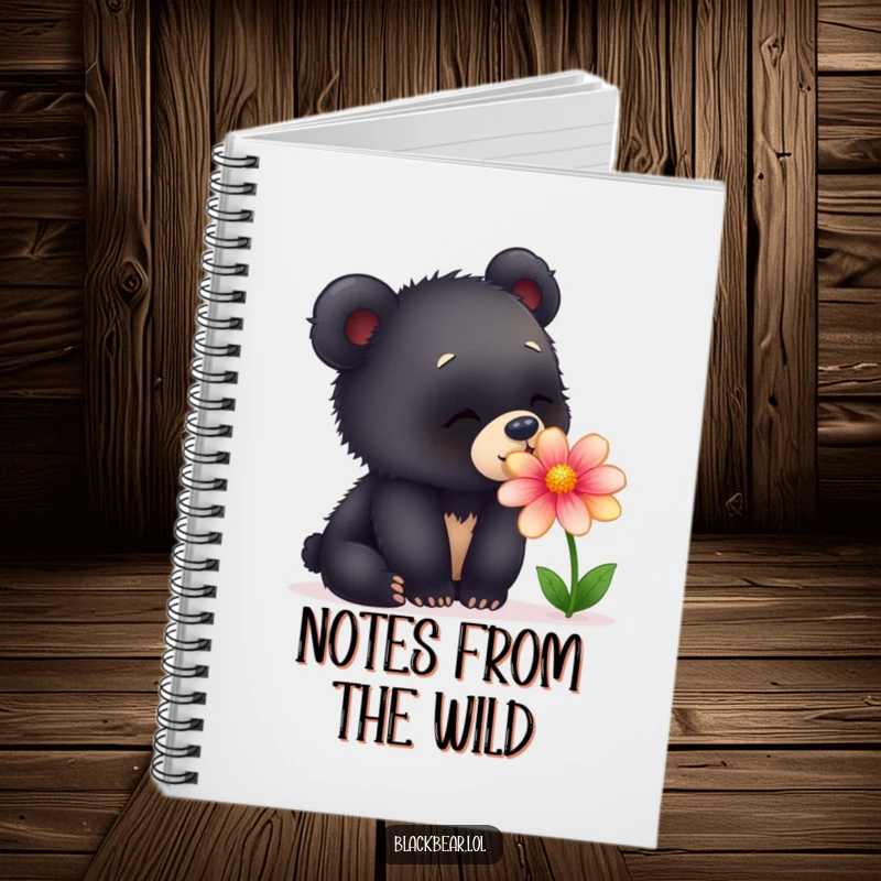 Funny notebook with a cover featuring a young black bear cub curiously sniffing a colorful flower, evoking delight and nature.