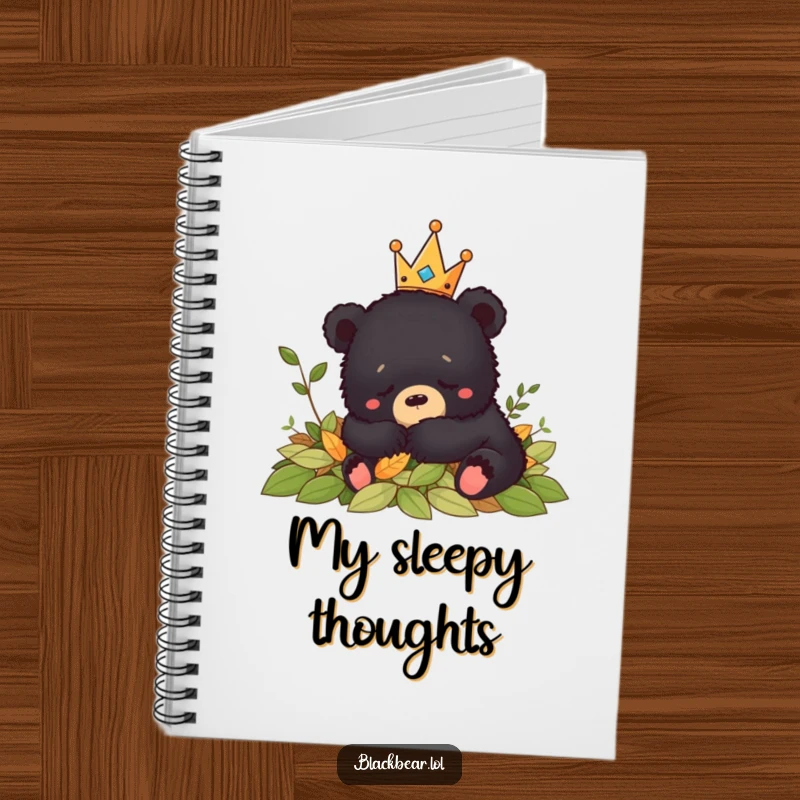Funny crowned black bear cub napping peacefully in leaves, featured on the cover of this humorous notebook.