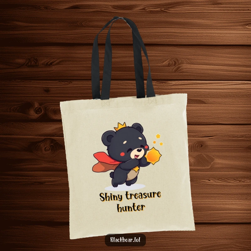Funny tote bag design of a black bear cub in a regal cape, playfully lunging towards a shiny object with great enthusiasm.